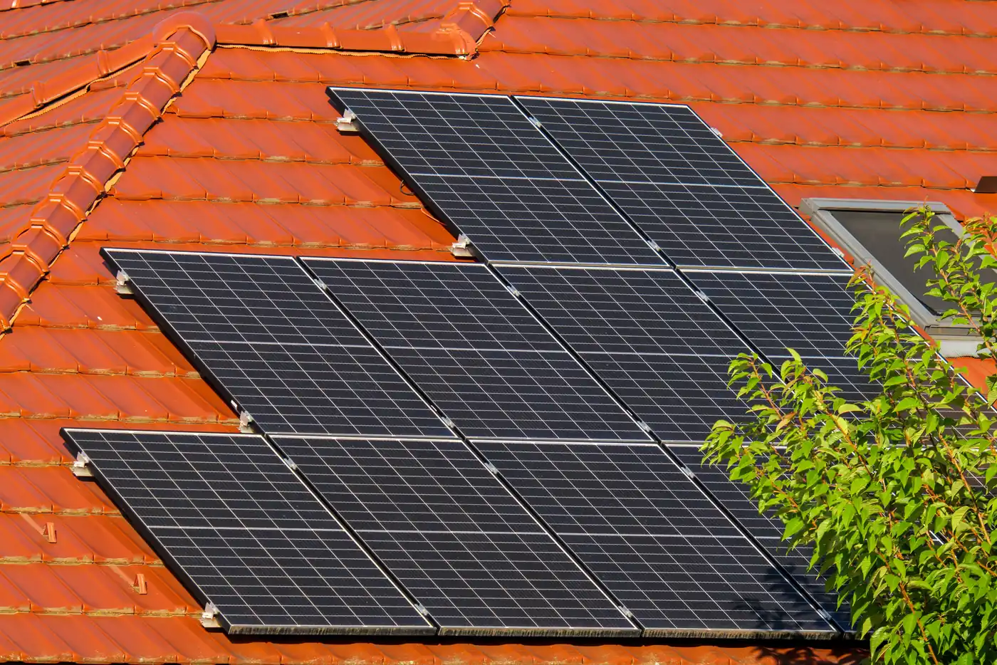 Schwarze Solarmodule in versetzten Reihen auf einem roten Ziegeldach mit Dachfenster (Grebin, Kreis Plön)