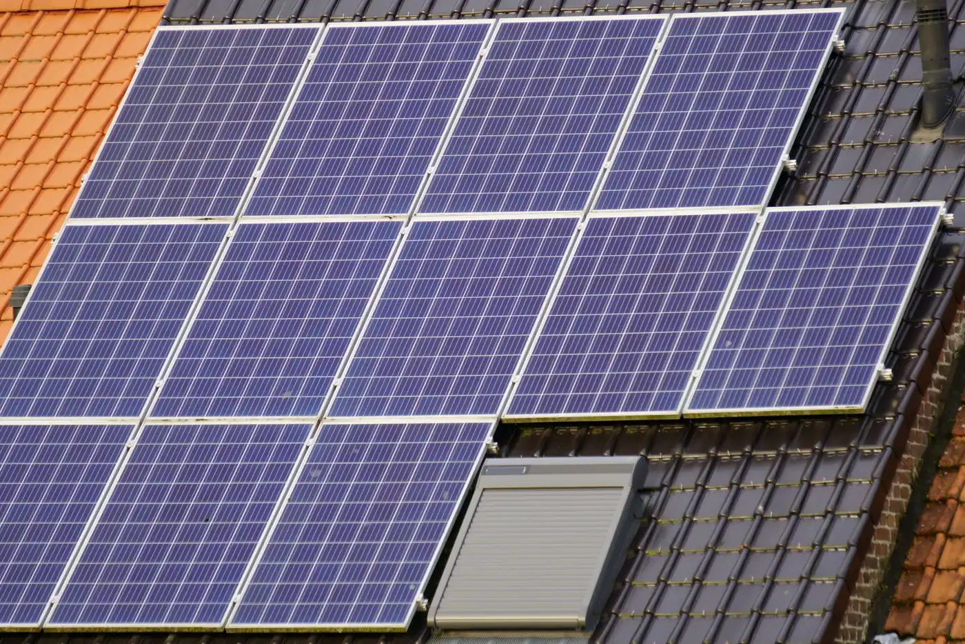 Blaue Solarmodule und ein Dachfenster auf einem dunklen Ziegeldach in Nahaufnahme (Thune, Stadt Braunschweig)