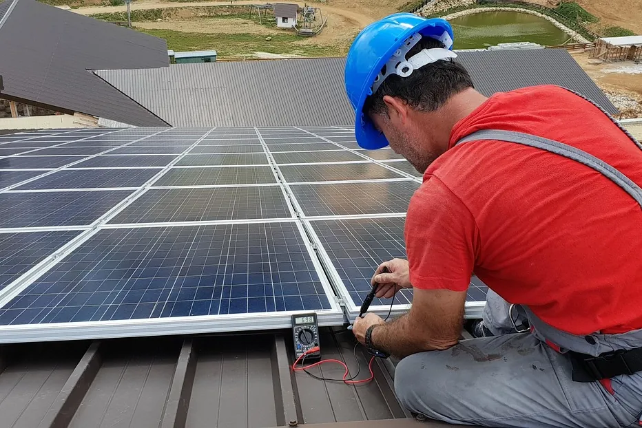 Techniker mit Helm und Sicherungsgurt misst die Spannung an Solarmodulen auf dem Dach (Emstek, Landkreis Cloppenburg)
