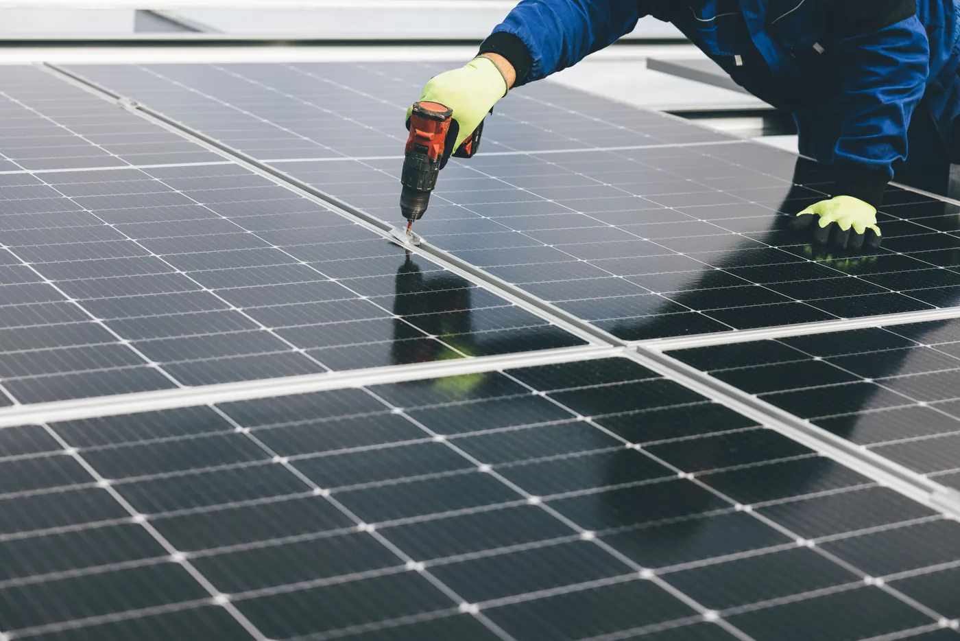 Monteur mit Handschuhen schraubt mit einem Akkuschrauber Modulklemmen zwischen Solarmodulen fest (Wittlingen, Landkreis Lörrach)