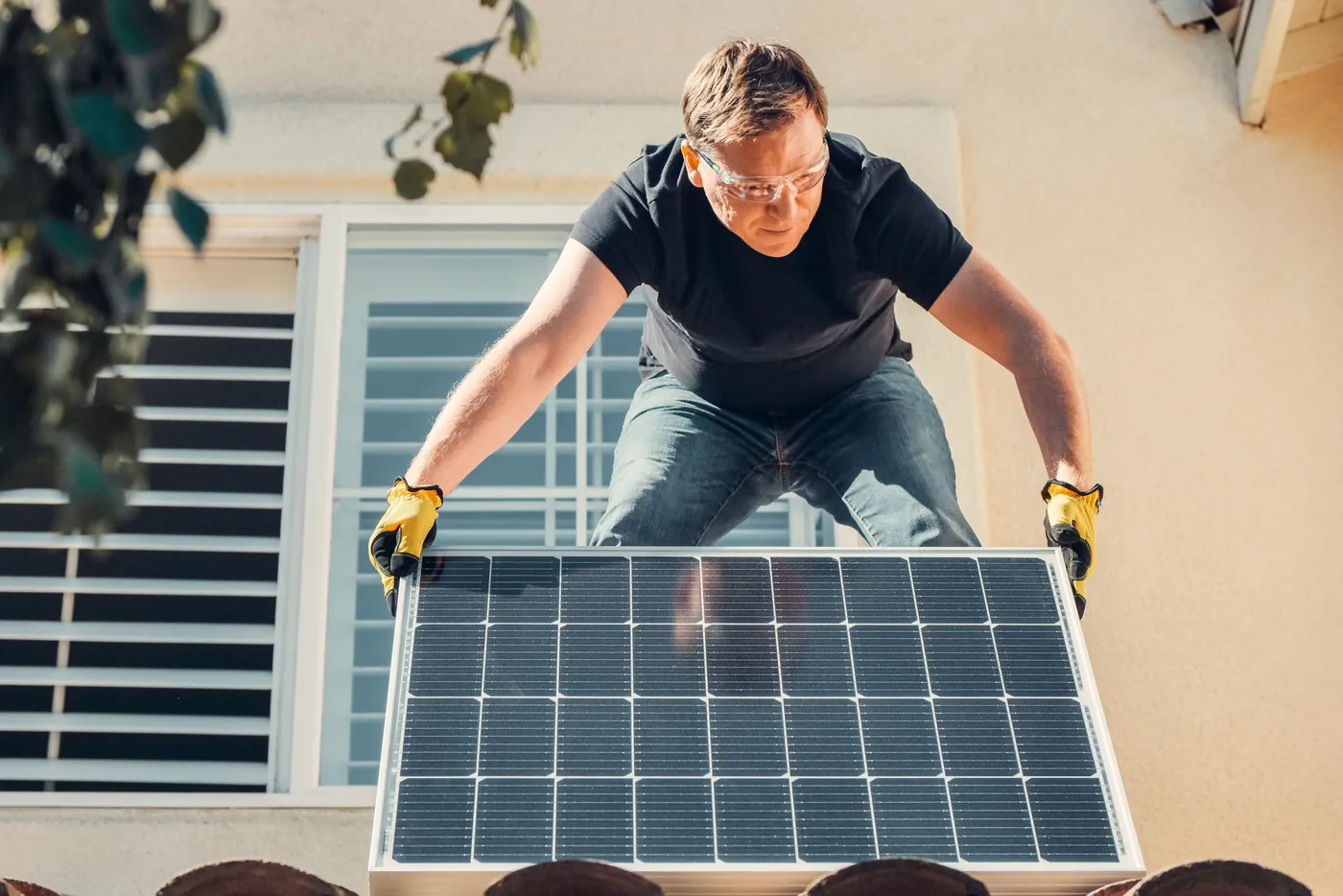Handwerker mit Schutzbrille hebt ein Solarmodul auf das Ziegeldach eines Hauses (Butzbach, Wetteraukreis)