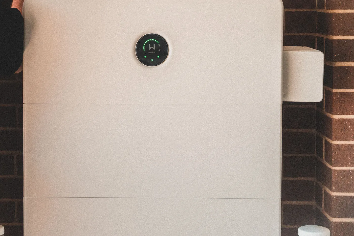 Weißer Heimbatteriespeicher mit Statusanzeige an einer Backsteinwand (Neubiberg, Landkreis München)