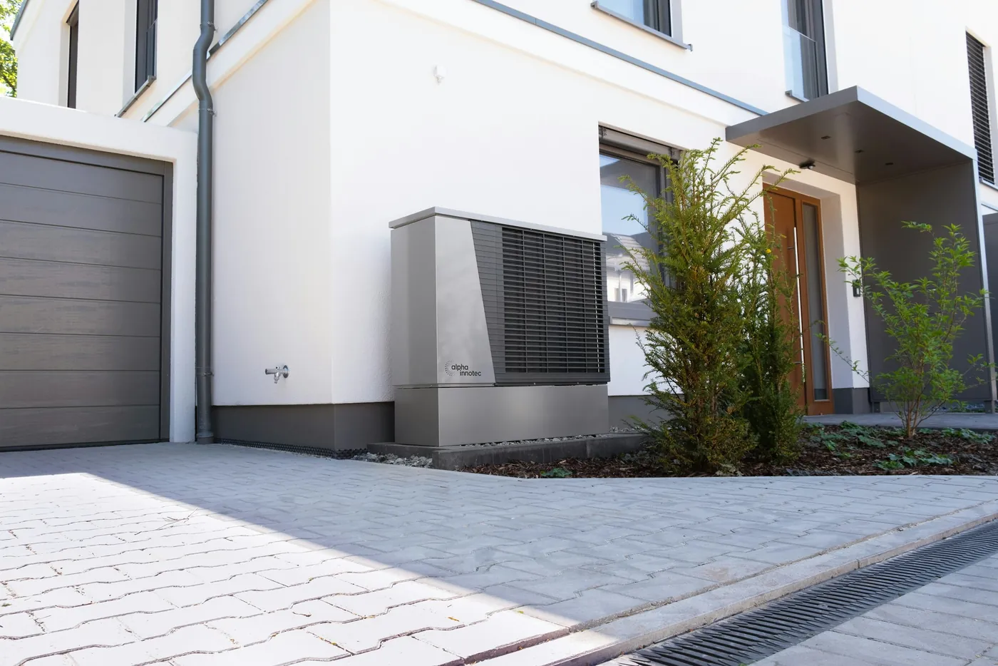 Graue Wärmepumpe vor einem modernen weißen Einfamilienhaus neben dem Garagentor