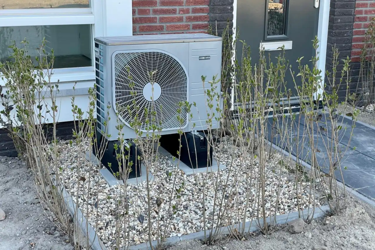 Wärmepumpen-Außeneinheit mit Ventilator im Kiesbeet vor einem Backsteinhaus