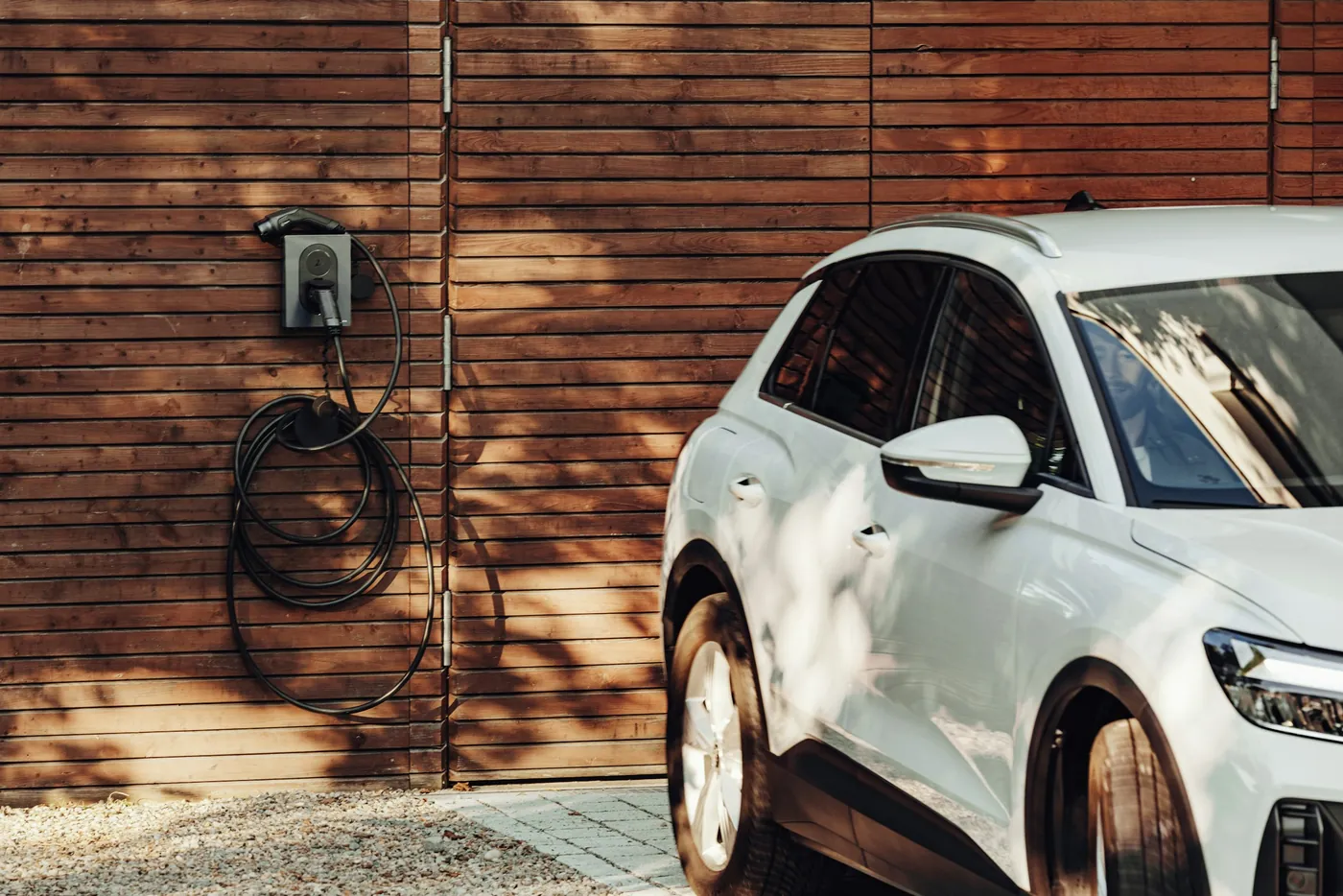Weißes Elektroauto neben einer Wallbox mit aufgerolltem Ladekabel an einer Holzfassade (Schwepnitz, Landkreis Bautzen)