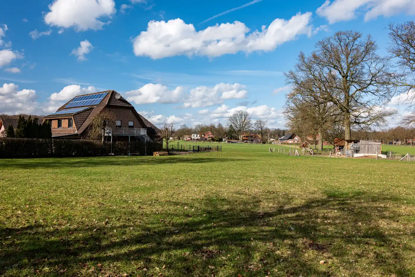 Einfamilienhaus mit Solaranlage am Rand einer weiten Wiese unter Wolkenhimmel (Haag, Landkreis Hof)